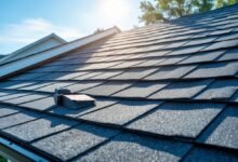 Close-up of a house roof with asphalt shingles under a clear blue sky, showing roofing tools nearby.
